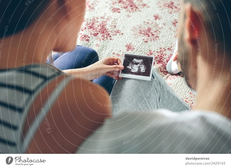 Couple looking at ultrasound of their baby sitting on bed Examinations and Tests Human being Baby Woman Adults Man Parents Mother Father Family & Relations