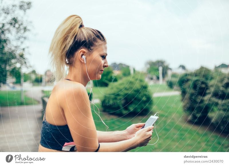 A woman in athletic attire is seen inserting earphones while exercising  outdoors. from Pikwizard