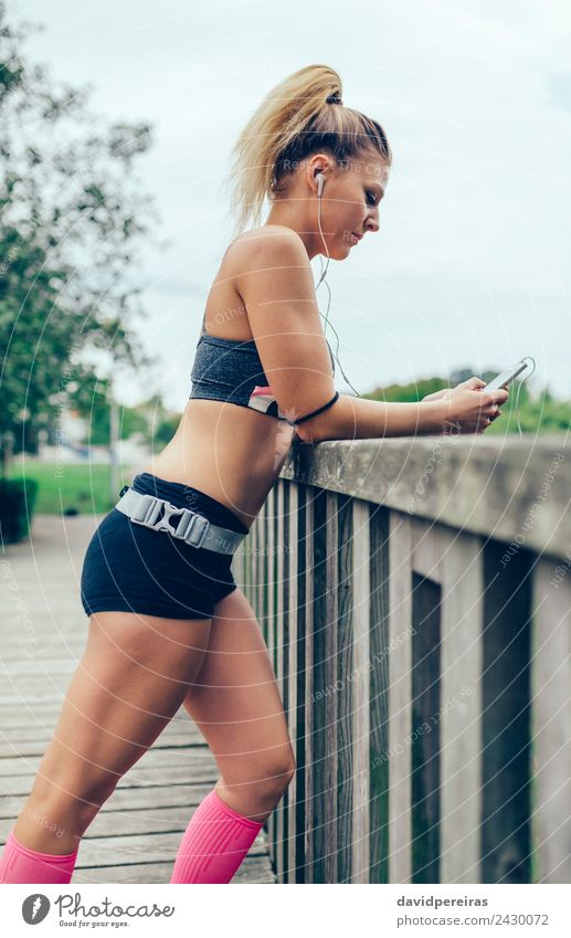 Woman in sports wear with earphones looking smartphone - a Royalty