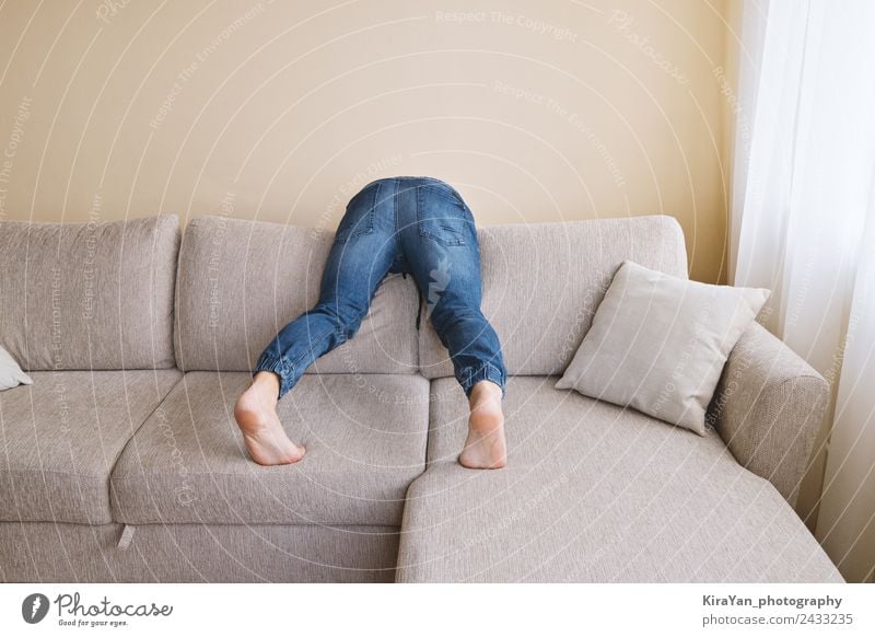 Man in jeans is cleaning behind sofa Lifestyle Relaxation Playing Furniture Sofa Hooligan Adults Father Bottom Feet Clothing Jeans Sadness Clean Stress Cozy