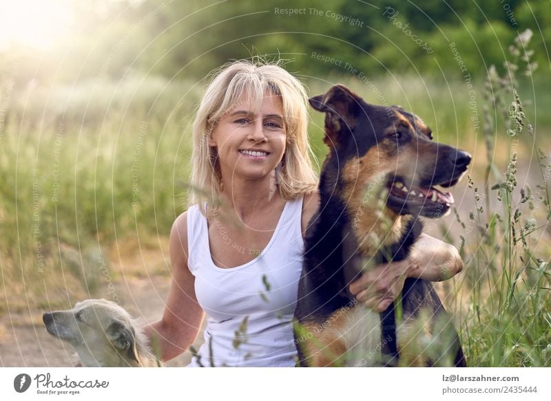 Pretty blond woman with her two dogs Happy Face Summer Woman Adults Friendship 1 Human being 45 - 60 years Animal Grass Meadow Blonde Pet Dog Smiling Love Sit