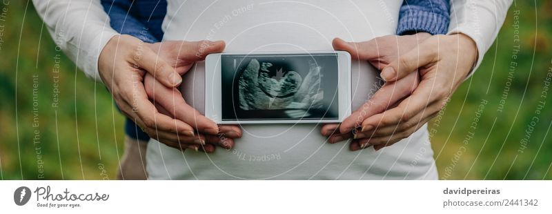 Man showing ultrasound over his wife's belly Lifestyle PDA Technology Human being Baby Woman Adults Parents Mother Couple Hand Authentic Pregnant panoramic