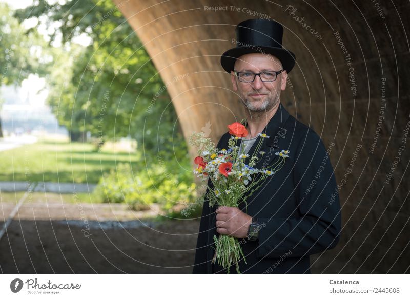 Man in tails with bouquet and top hat looks into camera Masculine 1 Human being Landscape Summer Tree Flower Grass Poppy Cornflower Meadow flower Wall (barrier)