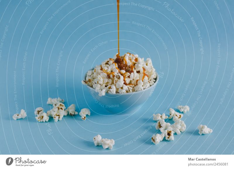 Bowl with popcorn and caramel sauce on blue background Grain Candy Nutrition Eating Leisure and hobbies Table Party Event Feasts & Celebrations Watching TV