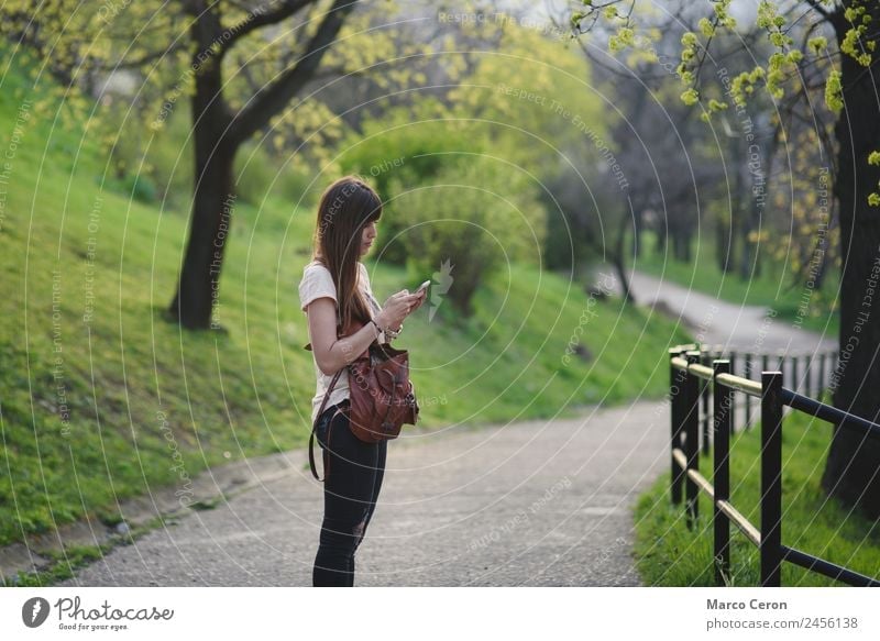 Attractive young woman having fun outside in a park. Caucasian girl with long brown hair checking her mobile Lifestyle Happy Beautiful Relaxation Calm