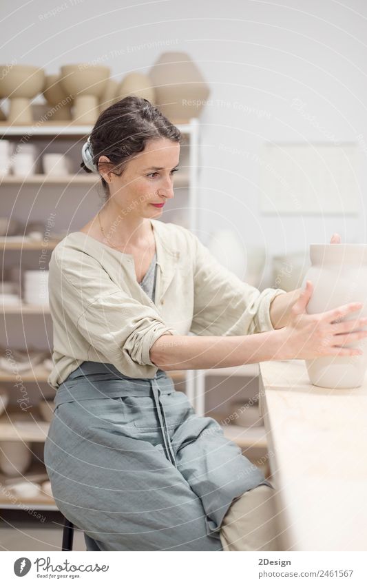 Young female sitting by table and making clay or ceramic mug Crockery Leisure and hobbies Handcrafts Table Work and employment Profession Craftsperson Workplace