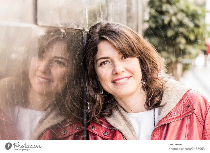 Woman smiling while leaning on wall outdoors Happy Business To talk Human being Adults Face 1 Jacket Leather Listening Smiling Stand Happiness Red Success Might