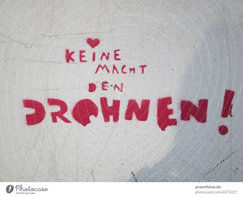 Graffiti: No power to the drones Gunpoint Weapon Peace Wall (barrier) Wall (building) Aircraft Sign Characters Aggression Red Revenge Force Politics and state