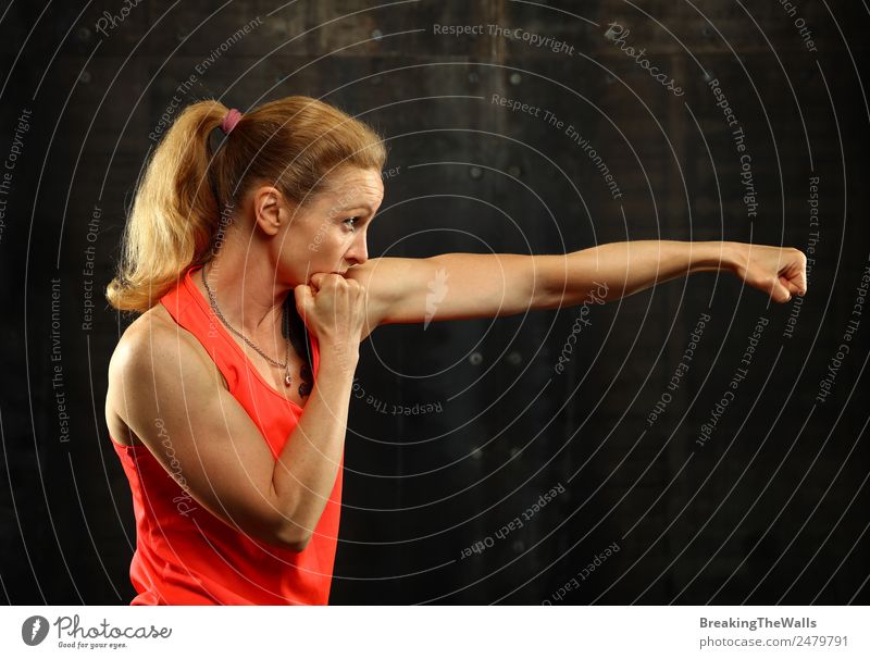 Close up side view profile portrait of one young middle age athletic woman shadow boxing in sportswear in gym over dark background, looking away Lifestyle