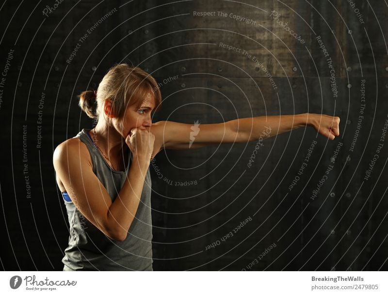 Close up side view profile portrait of one young middle age athletic woman shadow boxing in sportswear in gym over dark background, looking away Lifestyle