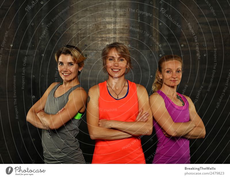 Close up front portrait of three young and middle age athletic women in sportswear in gym over dark background, looking at camera Lifestyle Athletic Fitness
