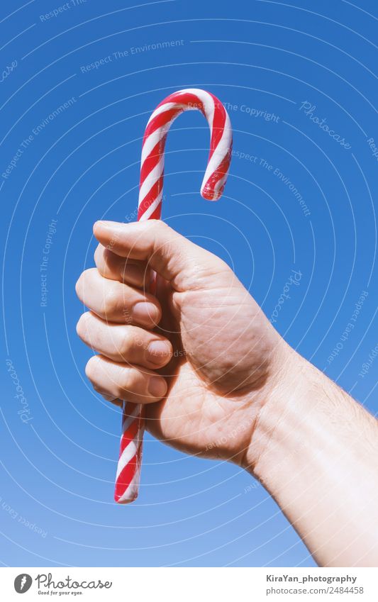 Man's hand holds traditional Christmas striped candy cane Design Winter Decoration Feasts & Celebrations Christmas & Advent New Year's Eve Adults Hand Sky