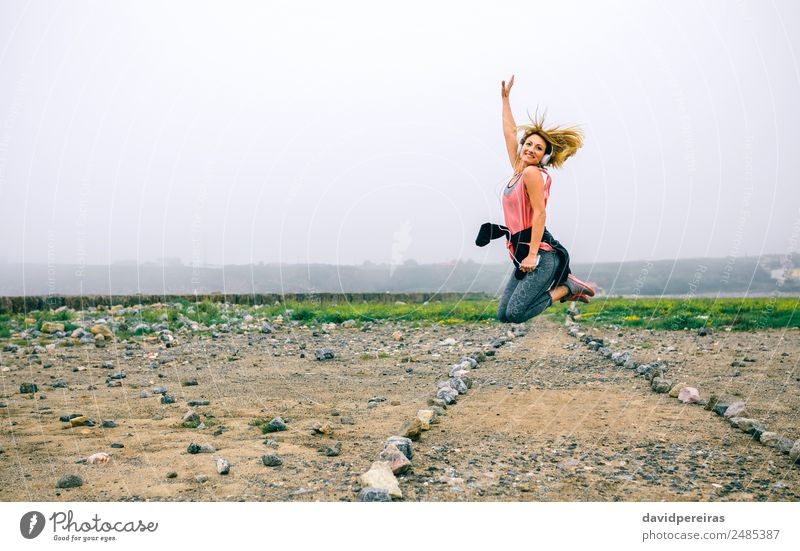 Young sportswoman jumping on the road Lifestyle Joy Happy Beautiful Music Sports Success Telephone PDA Human being Woman Adults Hand Landscape Fog Street