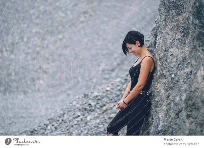 beautiful brunette short hair girl leaning on gray rock wall outdoors smiling happy attractive background black breathing caucasian day fashion female freedom
