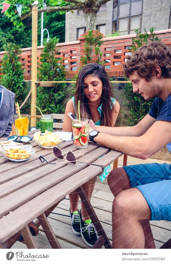 Young happy couple looking smartphone outdoors in summer Vegetable Fruit Beverage Lifestyle Joy Happy Leisure and hobbies Summer Garden Table Telephone PDA