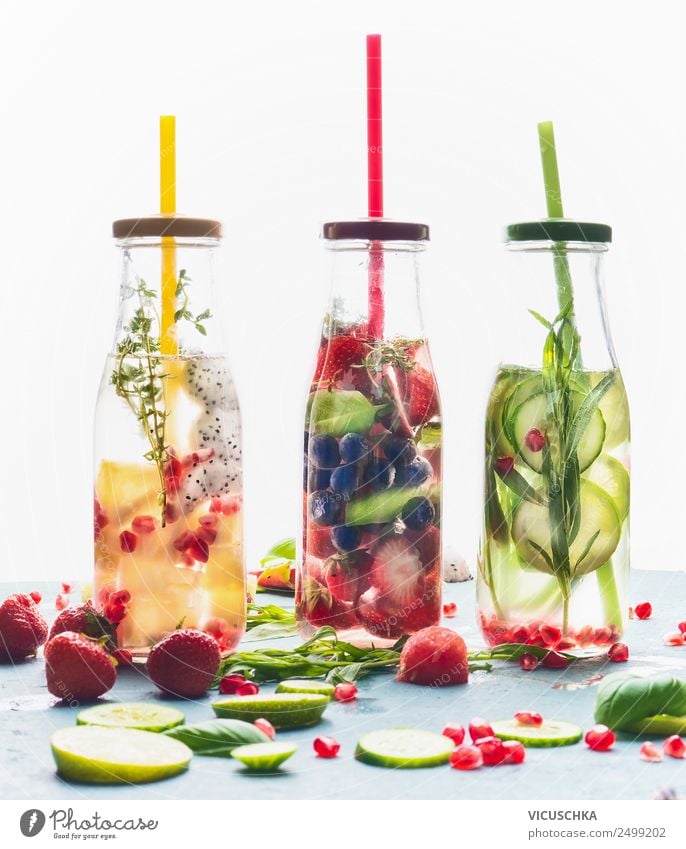 Infused water in bottles with drink straw and ingredients on white background, front view. Water Flavored with fruits, berries and herbs. Summer drinks. Healthy and clean detox beverages.