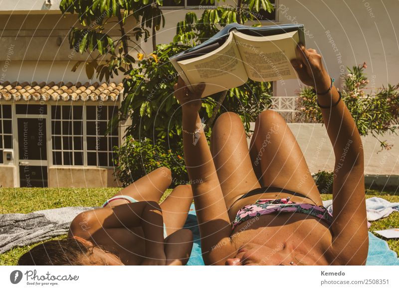 Mother reading a book with her little daughter in the pool while sunbathing. Sunny scene of summer. Family learning and reading on holidays. Lifestyle