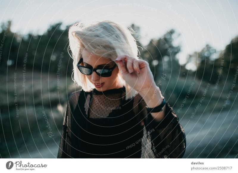 Blonde girl with sunglasses and black dress walking in nature with backlight Lifestyle Elegant Style Joy Vacation & Travel Trip Adventure Sun Human being
