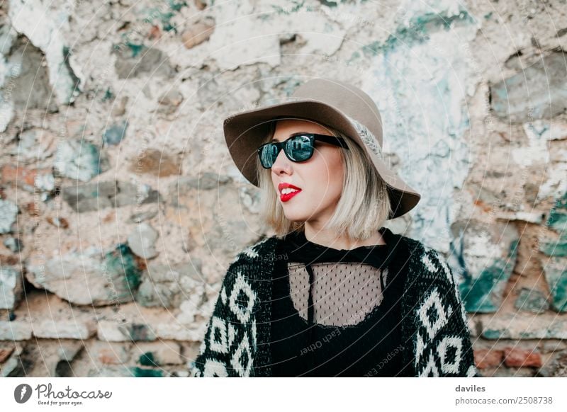 Portrait of blonde girl with hat and sunglasses looking away with a stone wall in the background. Lifestyle Shopping Luxury Elegant Style Joy Beautiful Face