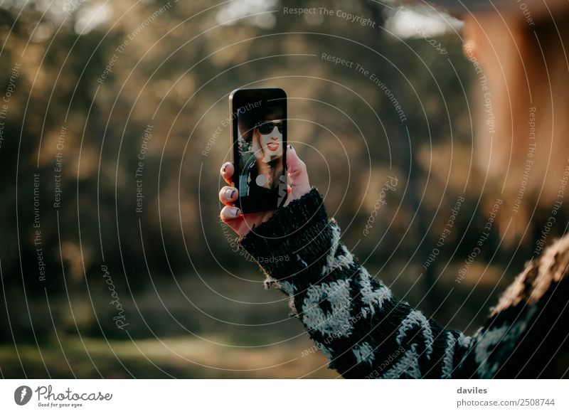 Woman holding a mobile phone to take a selfie photo outdoors. She appears in the device screen. Lifestyle Elegant Style Relaxation Leisure and hobbies Trip