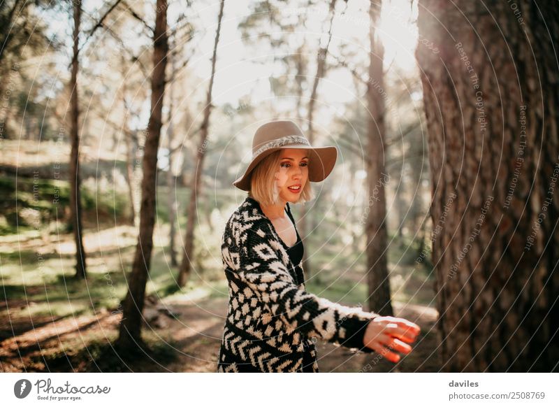 Woman walking in the forest at sunset and reaching a tree trunk with the hand. Lifestyle Joy Leisure and hobbies Sun Human being Feminine Young woman
