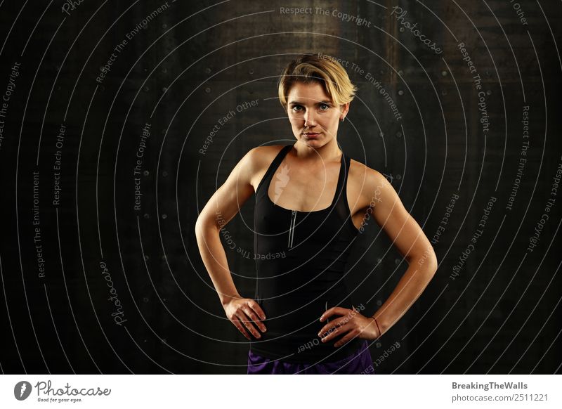 Close up front upper body portrait of one young athletic woman in sportswear in gym over dark background, looking at camera Lifestyle Sports Fitness