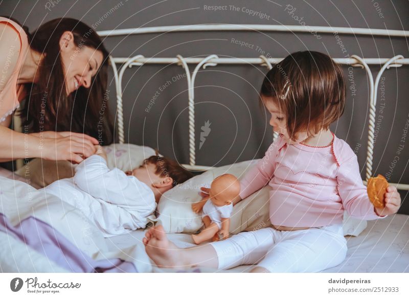 Happy little girl holding doll and cookie while woman playing with a boy over the bed. Weekend family leisure time concept. Eating Breakfast Lifestyle Joy