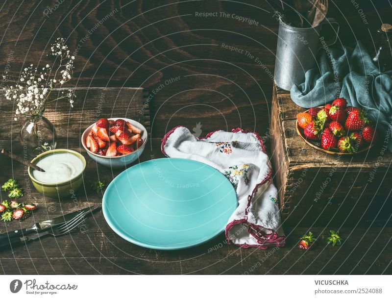 Empty blue plate on dark rustic wooden kitchen table with strawberries and yogurt in bowls. Country style food background with berries , still life. Place for your design, recipes , text or products