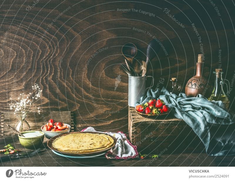Country still life with homemade crepes on dark rustic wooden kitchen table with strawberries and yogurt in bowls . country strawberry top view cream fresh