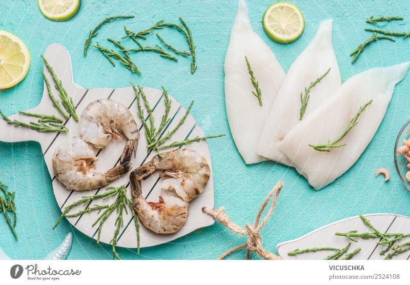 Raw prawn or shrimps and squids on light blue background, decorated with with seaweeds and lemon, top view, flat lay. Seafood cooking concept seafood above over