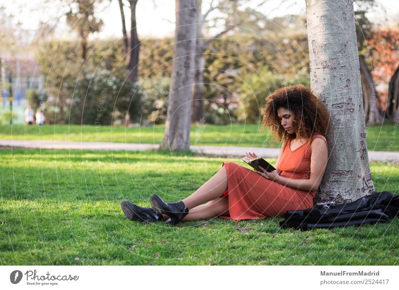 afro woman reading a book outdoors Lifestyle Happy Beautiful Leisure and hobbies Reading Summer School Study Human being Woman Adults Book Nature Tree Grass