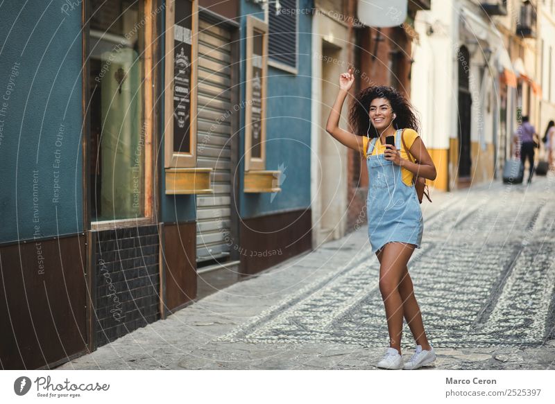 beautiful mixed girl listening to the music walking happy in the street african backpack black blue brown hair casual celular colours curly hair cute dancing