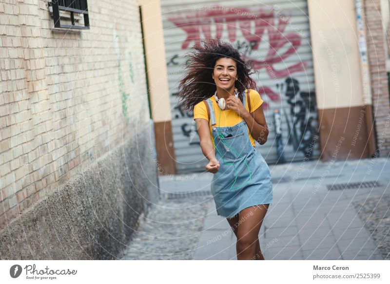 beautiful african girl casual dressed with headphones walking happy in the street listening music backpack black blue brown hair celular colours curly hair cute