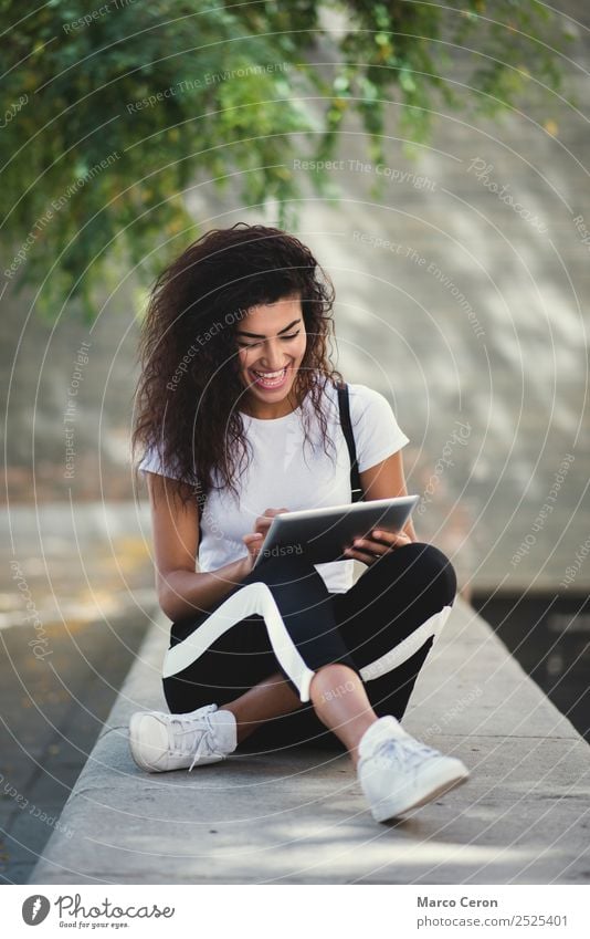 beautiful young woman sitting in the street while using happy her tablet. Mixed race attractive girl consulting social media in her device. african backpack