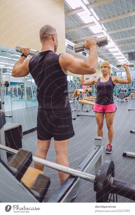 Female personal trainer helping a young man lift dumbells while working out  in a gym Stock Photo - Alamy