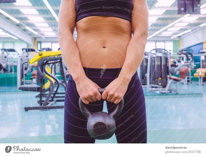Woman with slim waist and black sportswear holding kettlebell - a