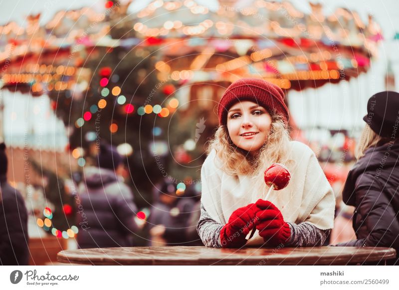 young happy girl eating caramel apple, walking at christmas city Shopping Happy Winter Decoration New Year's Eve Woman Adults Tree Town Fashion Hat Souvenir