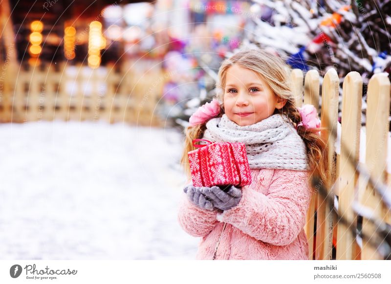 happy child girl holding christmas gift outdoor in winter city Shopping Winter Snow Decoration New Year's Eve Child Infancy Fur coat Scarf Smiling Bright Cute