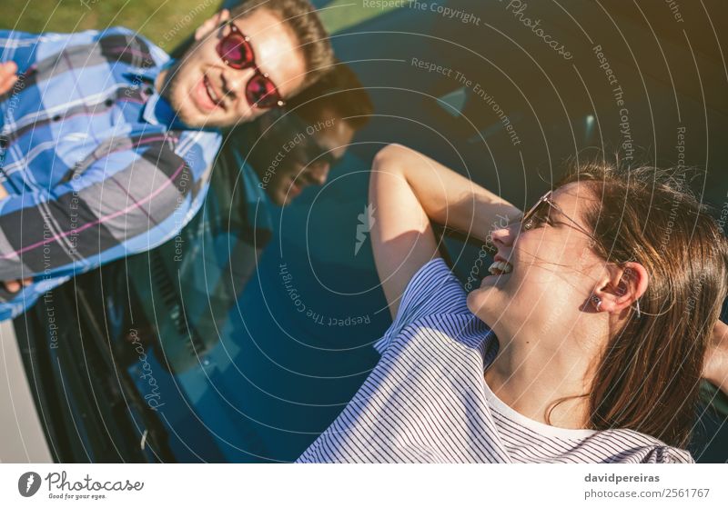 Young couple resting lying on windshield of car Lifestyle Style Happy Beautiful Relaxation Vacation & Travel Sunbathing To talk Human being Woman Adults Man