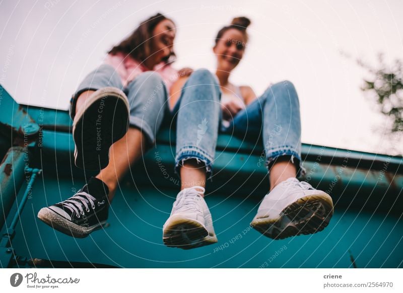 two cheeky women sitting on big container Lifestyle Joy Happy To talk Human being Woman Adults Friendship Jeans Sneakers Laughter Brash Funny Perspective young