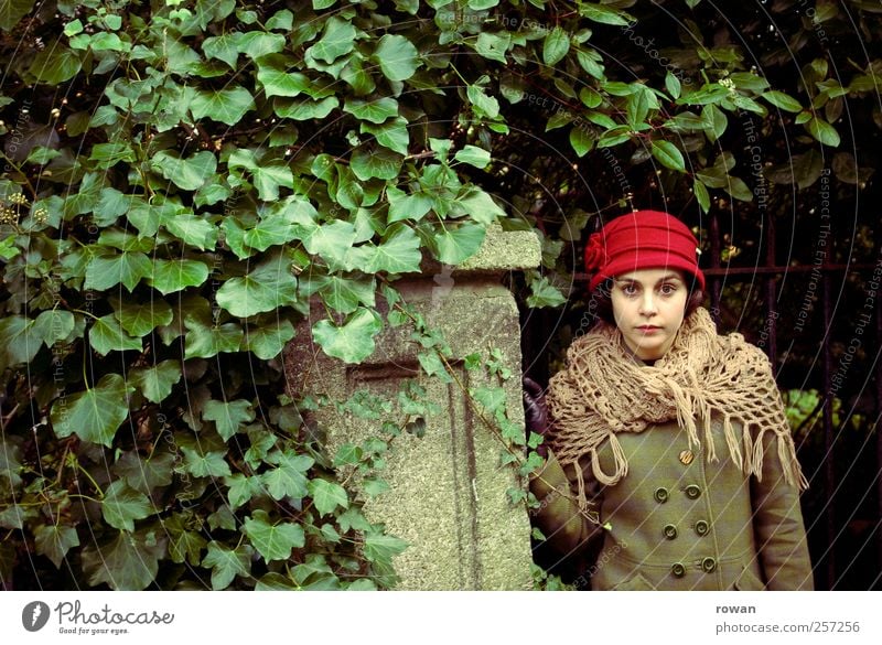 earnestness Human being Feminine Young woman Youth (Young adults) 1 Bushes Leaf Wall (barrier) Wall (building) Hat Red Green Ivy Overgrown Gate Garden