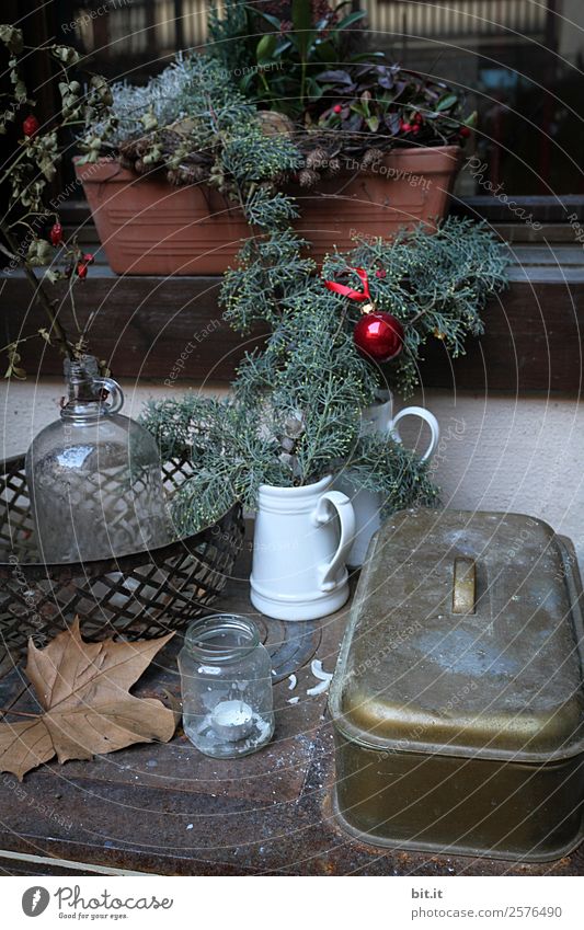 Rustic, beautiful Christmas decoration with twigs and a Christmas tree ball, on an old vintage table in winter during the Advent season. Christmas decorations with flower pot, tea light, glass vase, plants, cuttings on old stove, outside in the cold, icy garden.