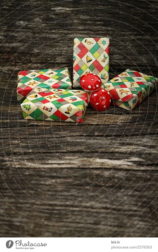 Surprise l many, colorful, wrapped Christmas parcels & mushrooms, lying on old rustic wooden table as decoration and ornamentation. Small Christmas presents wrapped in wrapping paper with a Christmas motif are waiting to be unwrapped under the Christmas tree.