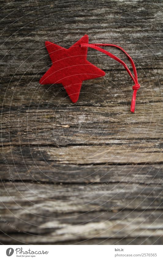 Merry Christmas. Red star of felt with ribbon, lies on old wood. Red poinsettia, as decoration on rustic brown wooden board. Felt fabric star as sign, blank, pendant, hanger on brown, rustic wooden table, text space.
