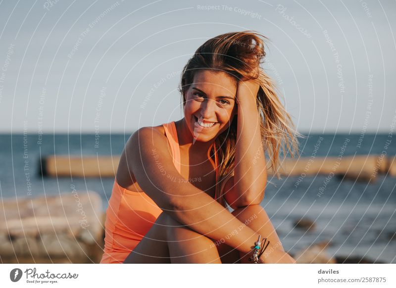 Beautiful woman with sports clothes, sitting on a concrete wall outdoors at sunset. Lifestyle Joy Body Wellness Relaxation Sun Ocean Sports Fitness