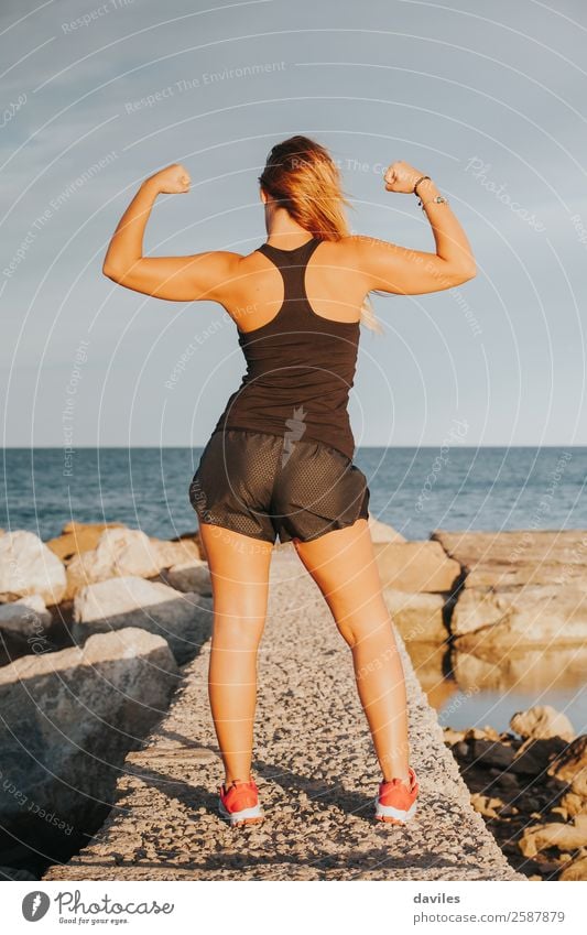 Young fitness woman flexing big strong biceps muscles towards the sun at  urban beach. Back view of female bodybuilder showing arms. Workout success  concept. Stock Photo