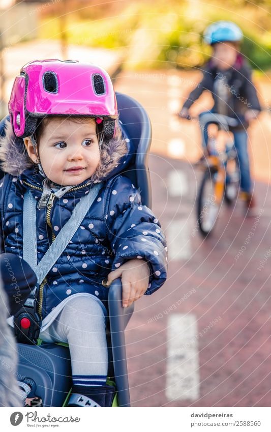 Lttle girl with helmet on head sitting in bike seat Lifestyle Leisure and hobbies Vacation & Travel Trip Winter Chair Child Baby Toddler Woman Adults