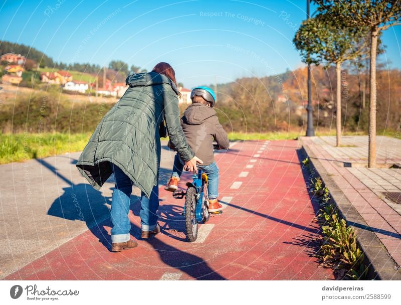 Back view of mother teaching her son to ride a bicycle Lifestyle Joy Happy Leisure and hobbies Playing Sun Winter Sports Cycling Child School Boy (child) Woman