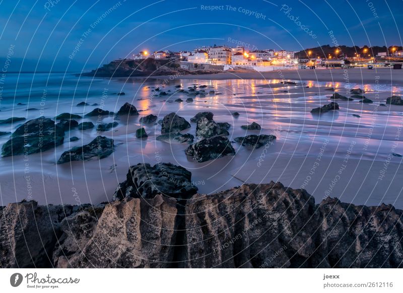 Rocks on the Atlantic beach at low tide with illuminated town in the background at dusk Beach Summer Ocean Portugal Praia das Maçãs Vacation & Travel