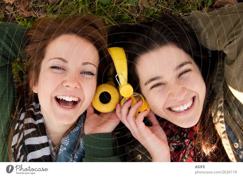 Two happy teenage girls lying on the grass sharing headphones to listen to music Joy Beautiful Winter Music Headset Human being Woman Adults Friendship